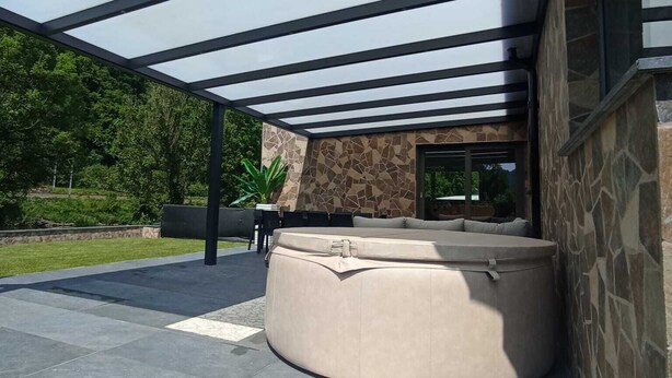 Un espace extérieur moderne, aménagé avec des sièges, un mur en pierre et une structure de plafond en verre.