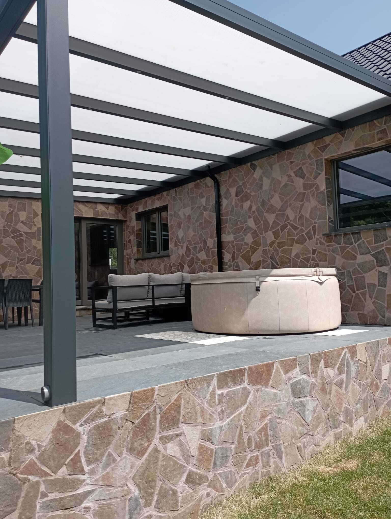 A covered outdoor seating area with stone walls, a bench, and a hot tub.