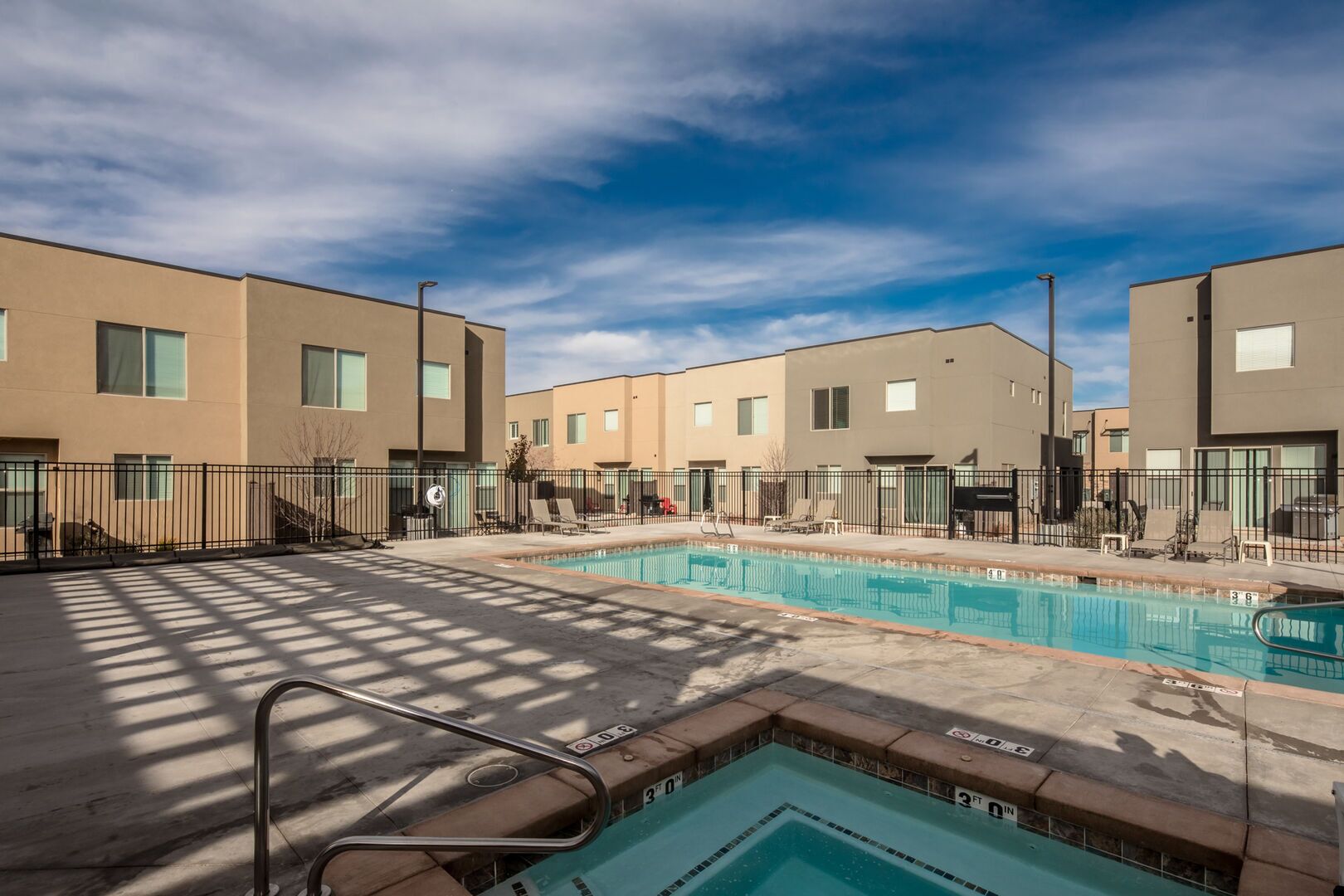 A modern building with a swimming pool, outdoor seating, and a clear sky.
