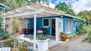 Une maison bleue avec un porche abrité, un coin repas et un jardin où poussent différentes espèces de plantes.