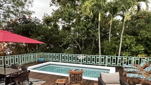 Un espace piscine avec une terrasse en bois, des chaises longues et un parasol rouge.