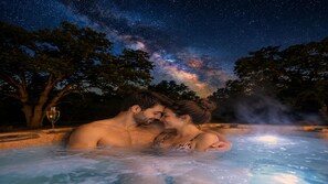 A couple in a hot tub with a night sky view, surrounded by trees.