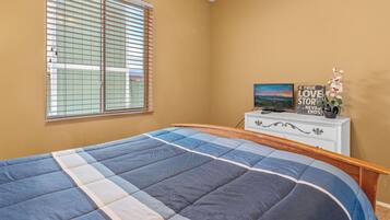 Een slaapkamer met een bed, een dressoir, een raam met zonwering en een decoratief object op het dressoir.