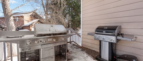 A stainless steel grill and oven set up outdoors, with a house in the background.