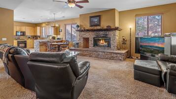 A spacious living room with a fireplace, leather sofas, a television, and a kitchen in the background.