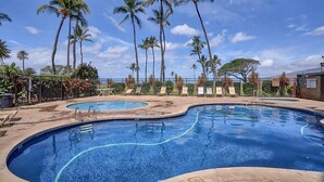 A swimming pool with two separate sections, surrounded by palm trees and lounge chairs. - Sea-rene & Tropical Vistas (Kihei)