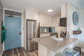 A modern kitchen with a stainless steel refrigerator, white cabinets, a built-in oven, and a large island with a sink. - Sea-rene & Tropical Vistas (Kihei)