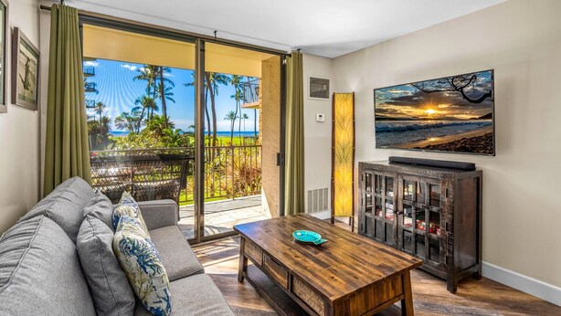 A living room with a sofa, coffee table, and a painting of a sunset. - Sea-rene & Tropical Vistas (Kihei)