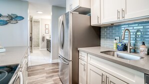 A modern kitchen with stainless steel appliances, light-colored cabinets, and a blue-tiled backsplash. - Sea-rene & Tropical Vistas (Kihei)