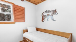 A single-bed room with a wooden headboard, a window with wooden shutters, and a wall mural of a bear. - Bear's Booth (Big Bear City)