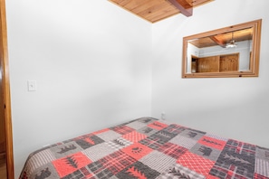 A bedroom with a bed, a wooden ceiling, a mirror, and a white wall.