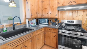 A kitchen with wooden cabinets, a stainless steel stove, a microwave, and a sink. - Bear's Booth (Big Bear City)