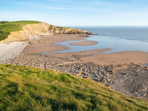 A coastal landscape with a pebbly beach, grassy areas, and cliffs. - The Hen House (Bridgend)