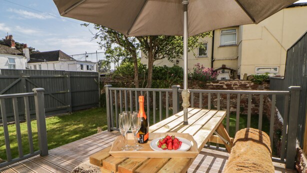 Een houten terras met een picknicktafel, een fles champagne en een schaal aardbeien.