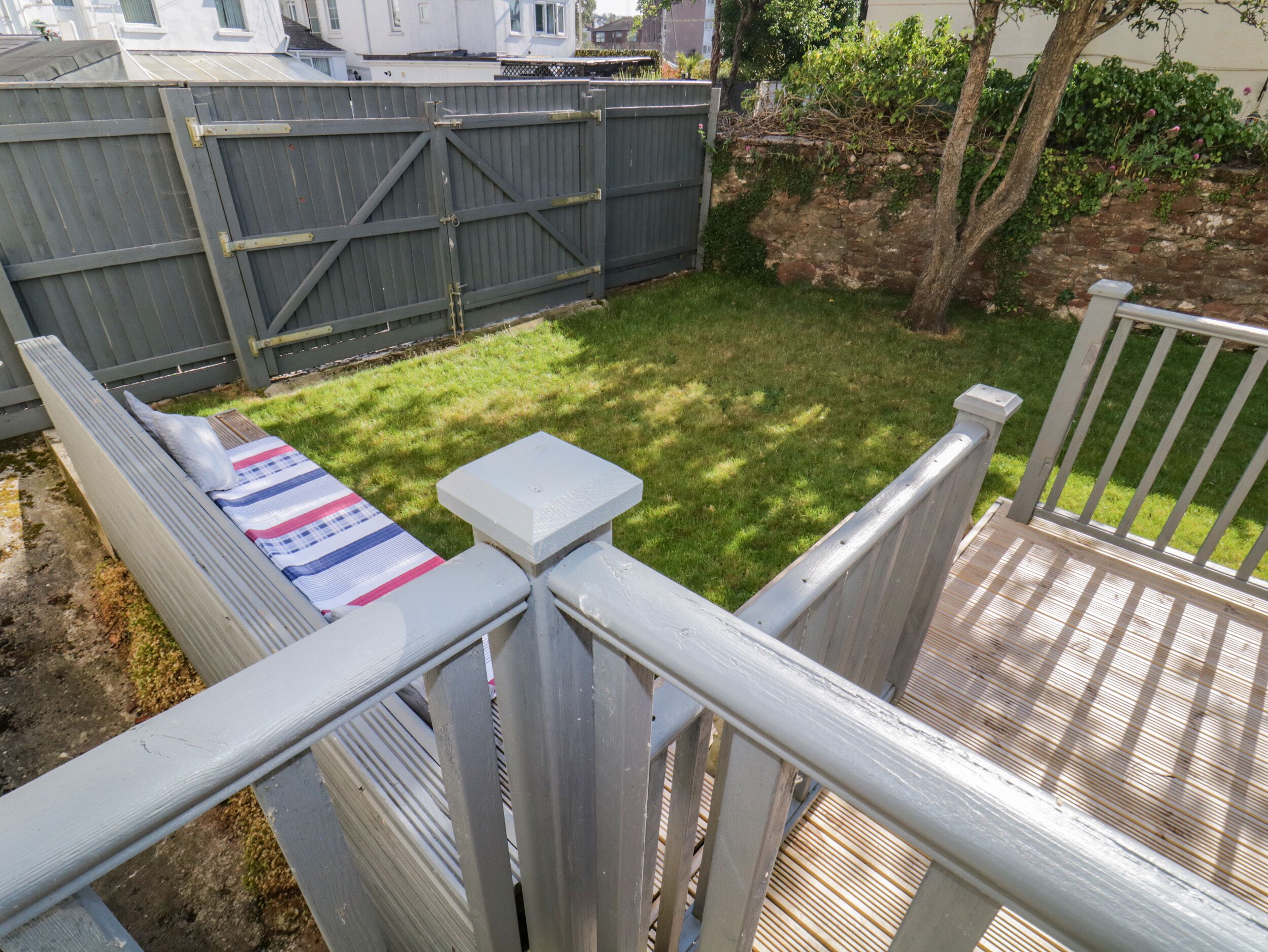 Ein Garten mit einer Holterrasse, einem eingezäunten Bereich und einem Rasen.