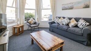 Een kamer met een grijze bank, een houten salontafel, een kleine fauteuil en een schilderij aan de muur.