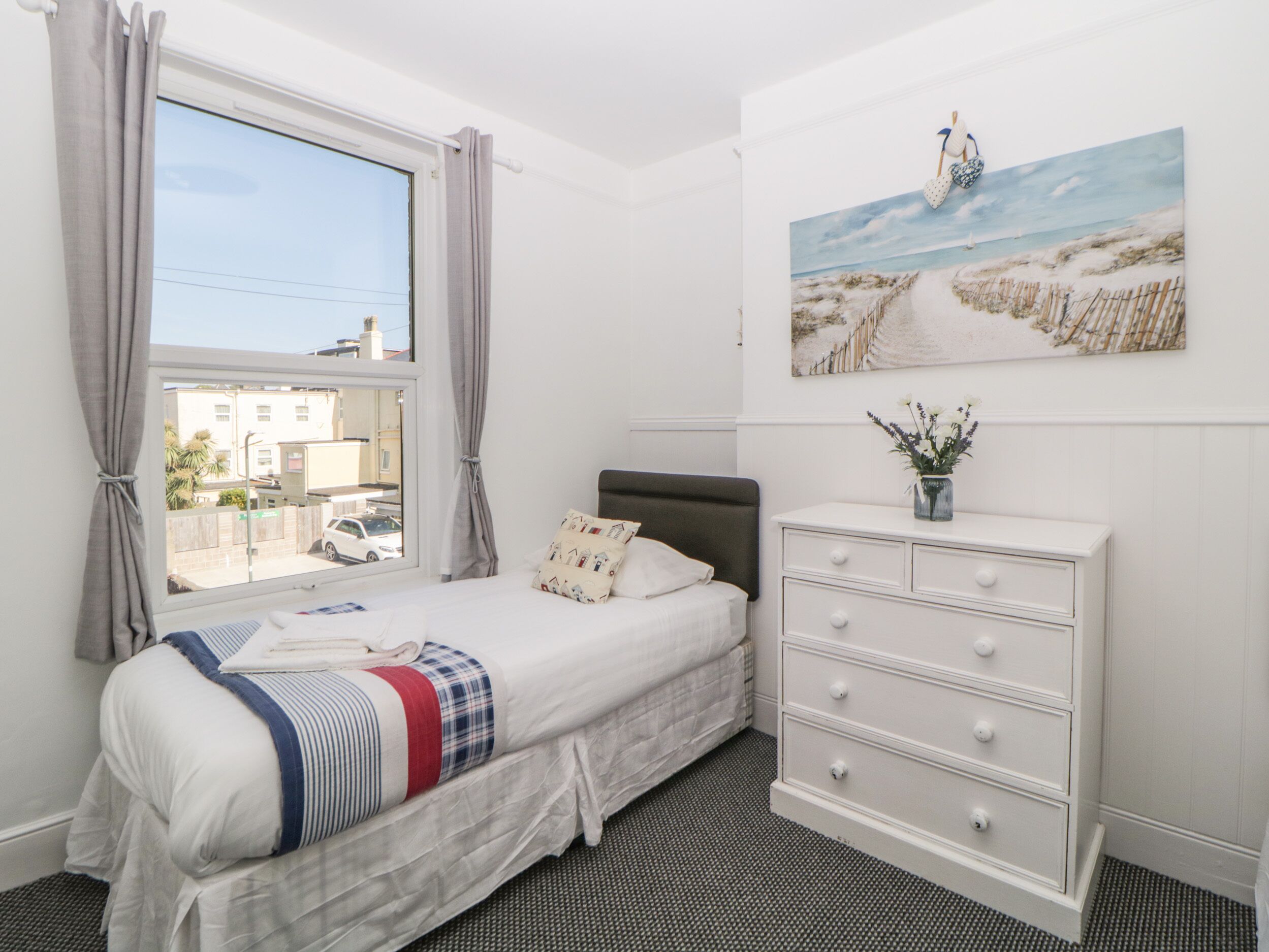 Un dormitorio con cama, cómoda, ventana con cortinas y un cuadro en la pared.