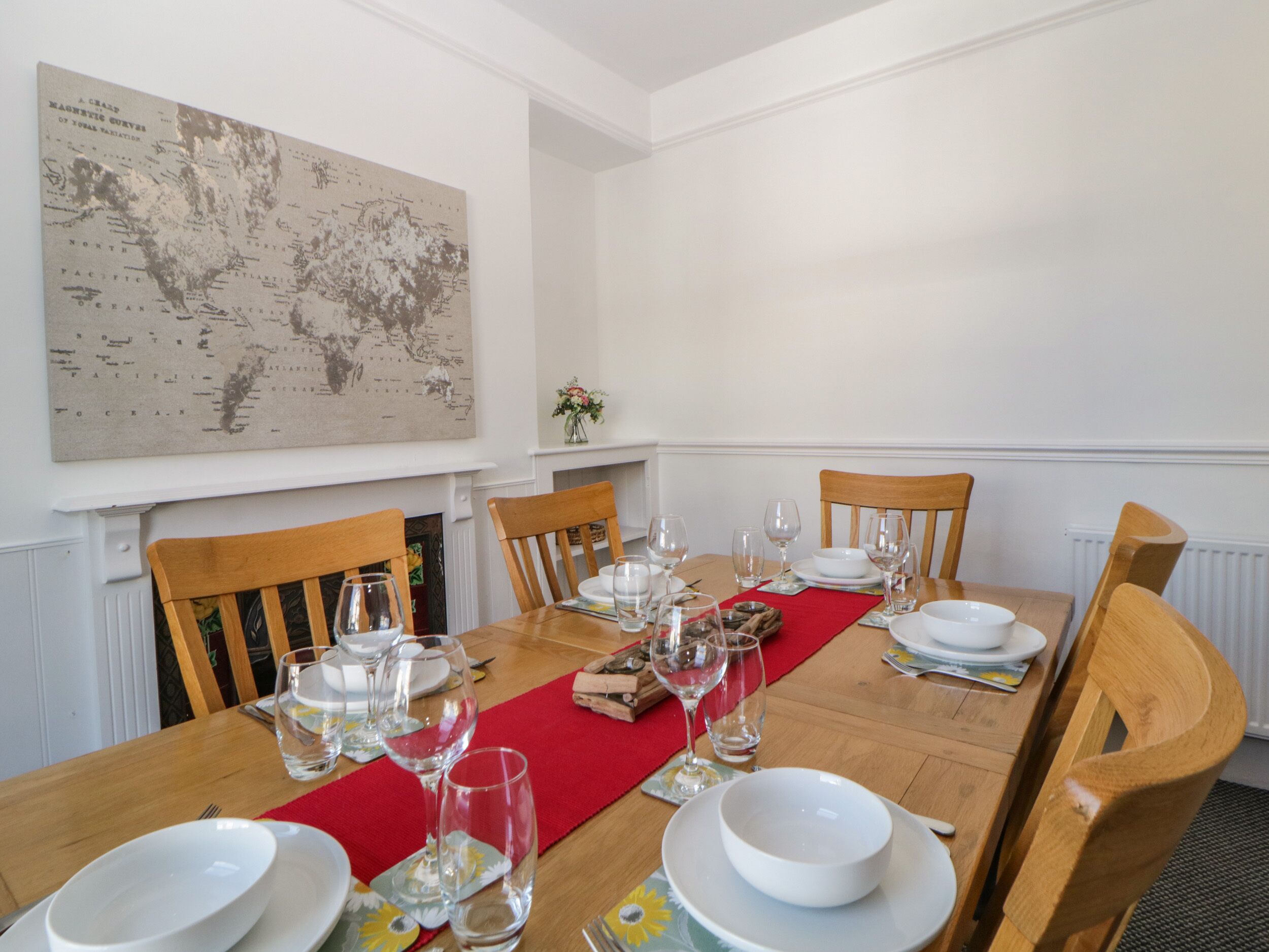 Un comedor con una mesa de madera dispuesta para seis personas, seis sillas y un gran mapa mundial en la pared.