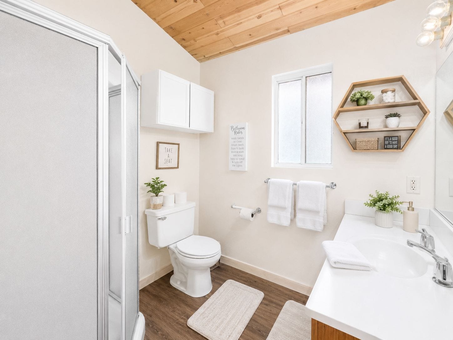 Une salle de bain moderne avec des toilettes, un lavabo et une douche. On y trouve des serviettes, une plante et un panneau accroché au mur.