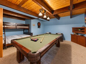A pool table in a room with a bunk bed, a dartboard, and a wooden cabinet.