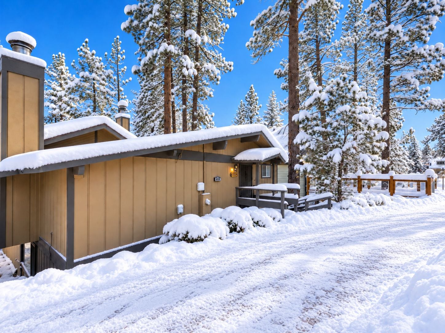 Un albergue cubierto de nieve con fachada de madera, un porche techado y un cielo azul despejado.