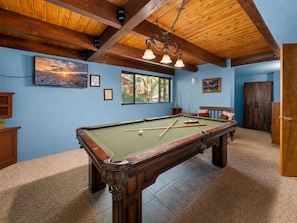 Een pooltafel in een kamer met blauwe wanden, houten balken in het plafond en een kroonluchter.