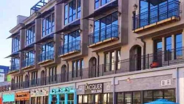 Un edificio de varios pisos con balcones y locales comerciales, incluyendo una peluquería Lacquer Nail Bar.