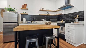 Una cocina moderna con una isla central, electrodomésticos de acero inoxidable, salpicadero blanco y negro y detalles de madera.