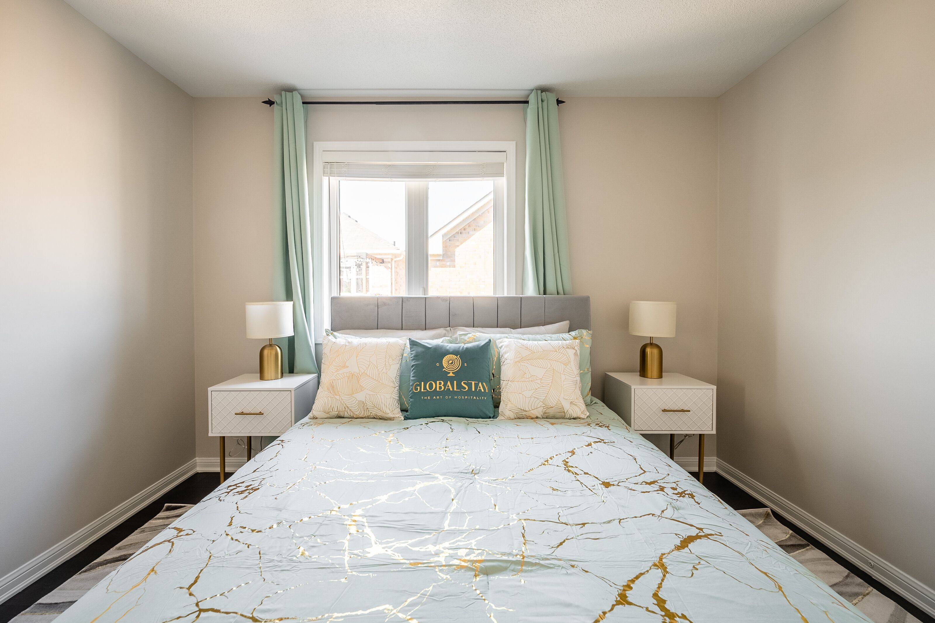A bedroom with a bed, two bedside tables, a window with curtains, and a headboard.