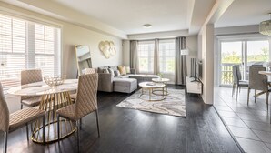 Una sala de estar moderna con comedor, un sofá modular y un ventanal con persianas.