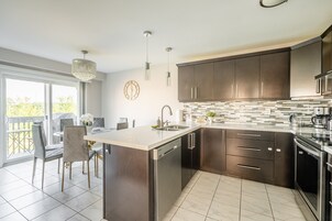 A modern kitchen with dark cabinets, a large island, and a dining area with chairs and a table.