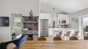 Une cuisine moderne avec des meubles blancs, des appareils en acier inoxydable et un coin repas comprenant une table et des chaises en bois.