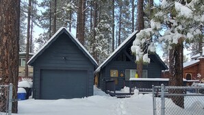 A cabin with a garage, surrounded by snow-covered trees. - Bearadise (Big Bear City)