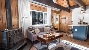 Una sala de estar acogedora con chimenea, un sofá, una mesa de centro y una zona de cocina con barra.