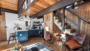 A modern kitchen with wooden cabinets, a central island, and a staircase leading to an upper level. - Bearadise (Big Bear City)