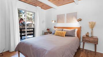 Un dormitorio con una cama grande, cabecera de madera, dos mesitas de noche con lámparas y vistas a una terraza de madera.