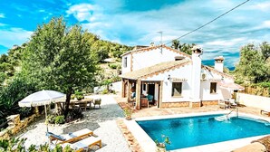Una villa blanca con piscina, rodeada de vegetación y un cielo despejado.