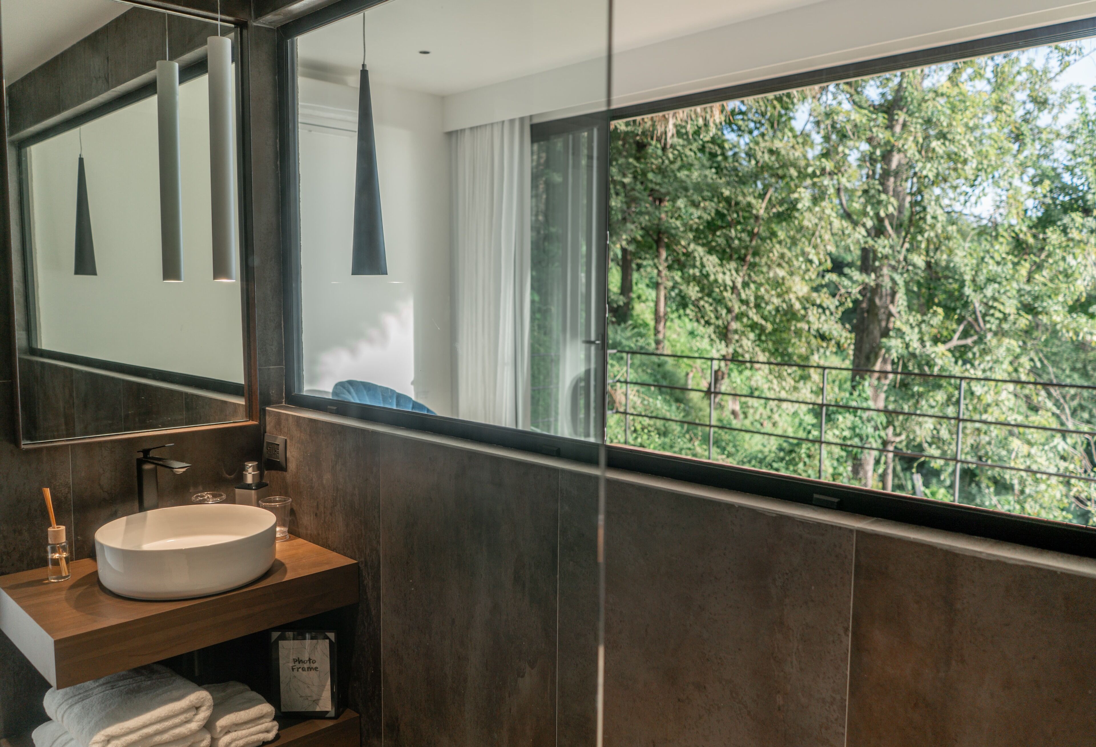 A modern bathroom with a large mirror, a round sink, and a view of trees through a window.
