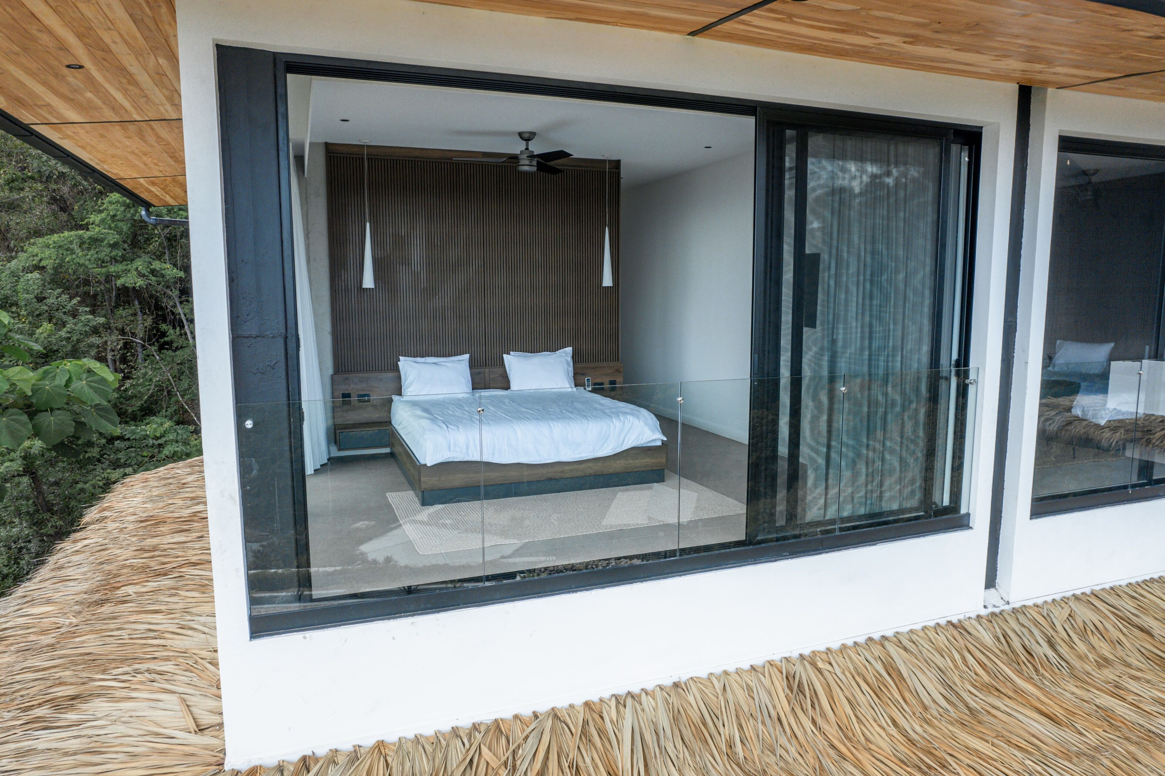 Un dormitorio moderno con un amplio ventanal corredero, una cama con ropa de cama blanca y un ventilador de techo.