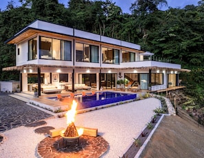 A modern two-story house with a swimming pool, outdoor seating, and a fire pit.