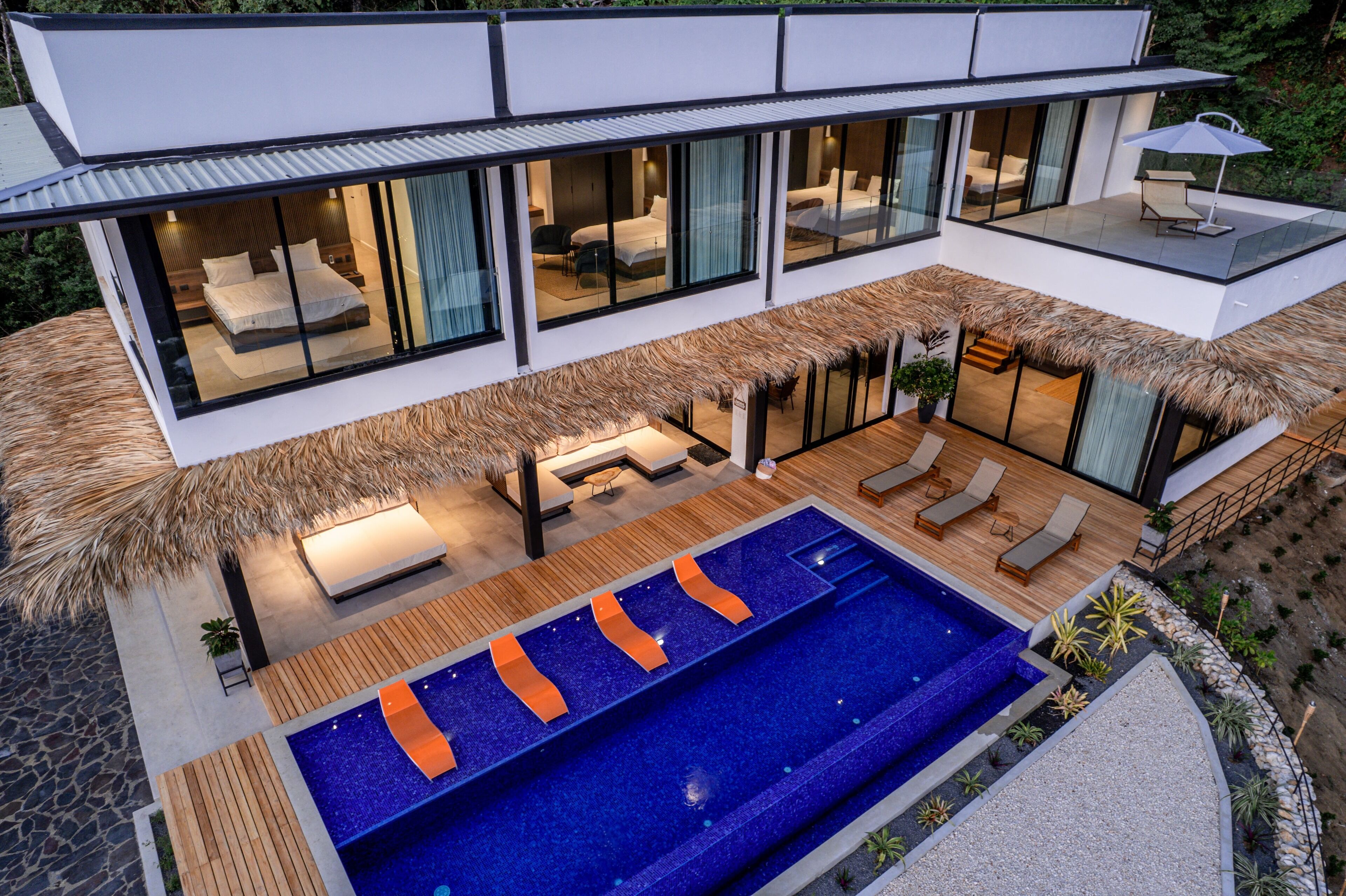 A modern villa with a large swimming pool, outdoor seating, and a glass-enclosed bedroom.