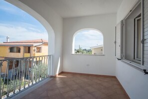 En balkon med flisegulv, gelænder i metal og et vindue med skodder.
