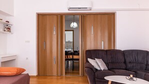 Una sala de estar moderna con un sofá marrón oscuro, una mesita blanca pequeña y un armario de madera con puertas correderas.