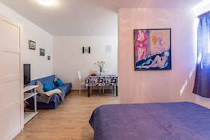 A room with a bed, a sofa, a dining table with chairs, and a TV.