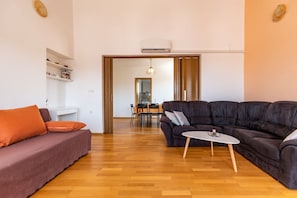 A modern living room with a dark brown sofa, a smaller sofa with orange cushions, a white coffee table, and a wooden floor.