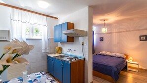 Een kleine kamer met een kitchenette, een bed en een nachtkastje met lamp.