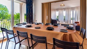 Comedor con una mesa larga dispuesta para seis personas, rodeada de sillas, y vista a zonas verdes al exterior.