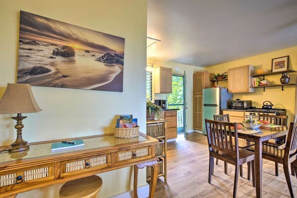 A spacious kitchen with wooden cabinets, a dining table with chairs, and a large painting of a beach scene. - Pineapple Cottage surrounded by coffee plantations (Holualoa)