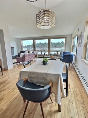 A spacious living room with a large window, a dining area with a table and chairs, and a view of a river. - Waterfront Home in Rapid River, MI (Rapid River)