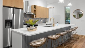 A modern kitchen with a central island, stainless steel appliances, wooden cabinets, and a large window.
